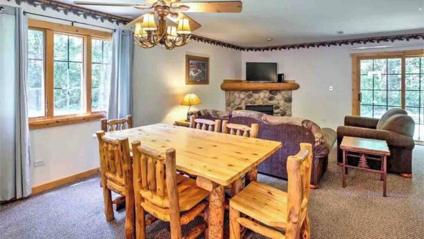 Een gezellige woonkamer met een houten eettafel, stoelen, een bank en een open haard.