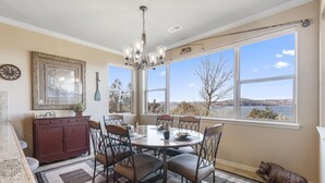 A dining area with a round table, six chairs, a chandelier, a large window with a view of a lake, and a bear statue.