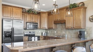 A kitchen with wooden cabinets, stainless steel appliances, a granite countertop, and pendant lighting.