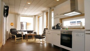 A modern kitchen with a built-in oven and dishwasher, wooden flooring, and a dining area with a table and chairs. - Swedish red vacation home "Isi" - Beach 500m - Holiday home on the Baltic Sea (Zierow)