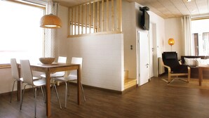 A room with a wooden dining table and chairs, a sofa, a TV mounted on the wall, and a window with curtains. - Swedish red vacation home "Isi" - Beach 500m - Holiday home on the Baltic Sea (Zierow)