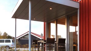 A covered outdoor seating area with chairs and a table, a red building, and a parked van in the background. - Swedish red vacation home "Isi" - Beach 500m - Holiday home on the Baltic Sea (Zierow)