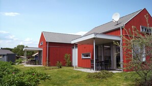 A red barn with a satellite dish, a covered patio with a table and chairs, and a well-maintained lawn. - Swedish red vacation home "Isi" - Beach 500m - Holiday home on the Baltic Sea (Zierow)