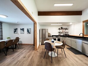 Une cuisine moderne avec des poutres en bois, des appareils électroménagers en acier inoxydable et une table de salle à manger ronde, assortie de chaises.