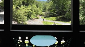 Ein überdachter Außenbereich mit Tisch und Stühlen, der auf eine üppige grüne Landschaft mit Bäumen und einem gewundenen Weg blickt.