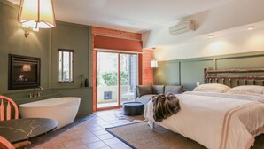 A modern bedroom with a large bed, a bathtub, and a dining area. - NEW! Signature Spa Suite with Fireplace & Den (Whittier)