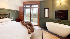 Una camera da letto con un letto grande, un bagno con una vasca freestanding e una porta scorrevole in vetro che dà su uno spazio esterno.