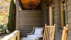 Un portico in legno con una ventola a soffitto, una sedia in metallo con cuscino e una poltrona a dondolo in legno.