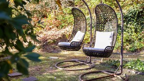 Twee rieten stoelen met kussens in een tuin.