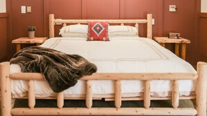 Een houten bed met hoofdeinde, twee nachtkastjes, een rood kussen en een dekbed.