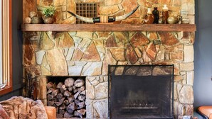 A stone fireplace with a mantel, a log storage area, a sofa, and a coffee table in a living room. - NEW! Romantic Loft Spa Suite with Fireplace & Den (Whittier)