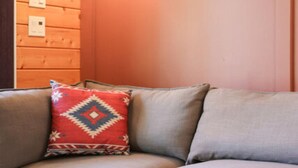 A corner sofa with a patterned pillow, a round table, and a wall-mounted light fixture. - NEW! Romantic Loft Spa Suite with Fireplace & Den (Whittier)