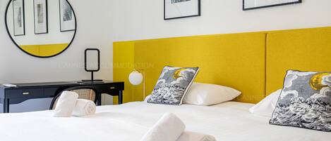 A hotel room with a bed, two pillows with wave designs, a desk with a lamp, and framed artwork on the wall.