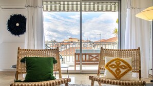 A balcony with wicker chairs, a glass table, and a view of buildings.