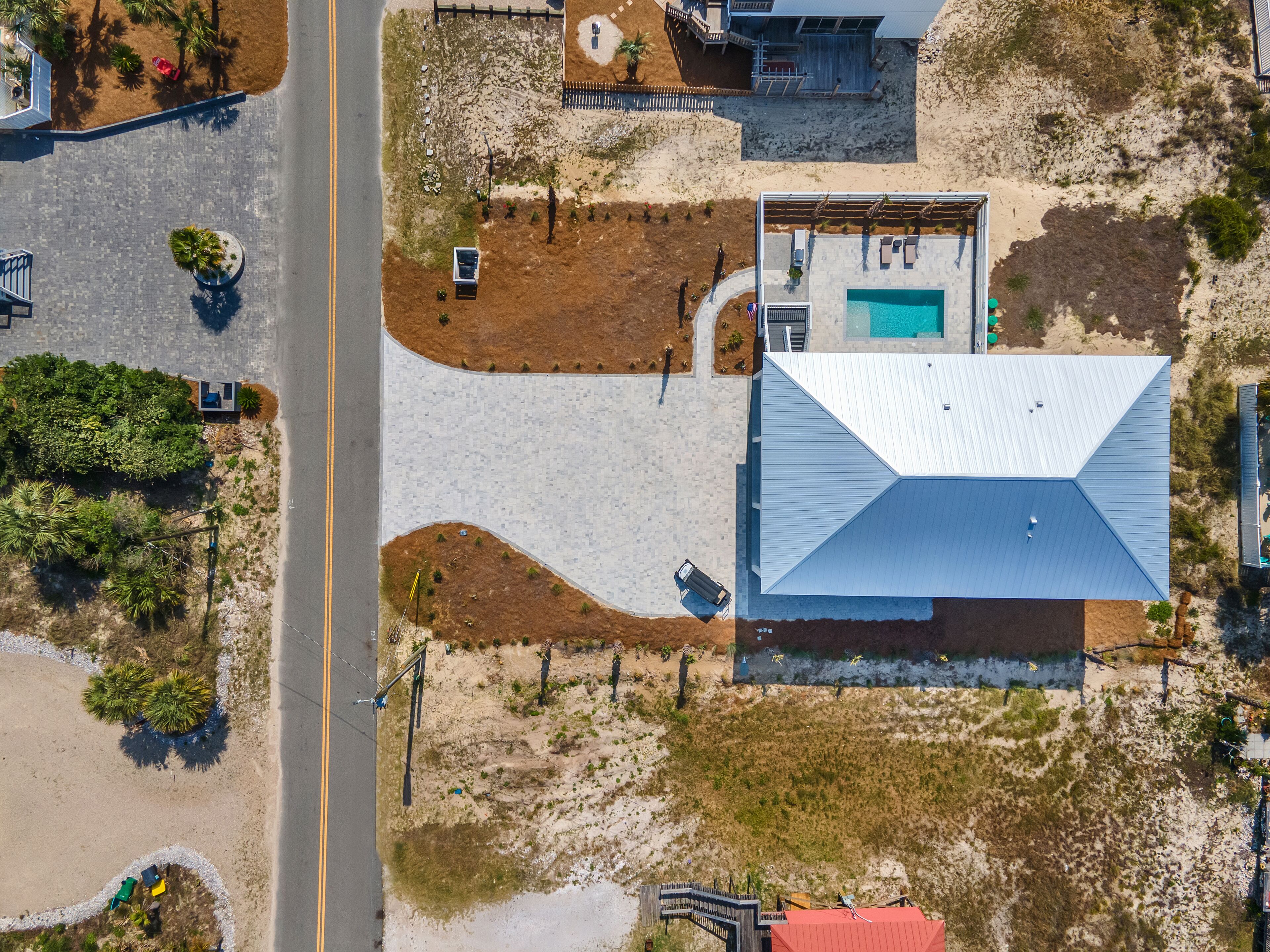 An aerial view of a property with a swimming pool, a large building with a sloped roof, and a road adjacent to the property.