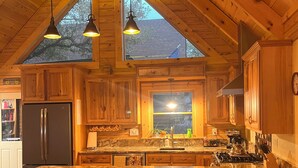A kitchen with wooden cabinets, a granite countertop, a stainless steel refrigerator, and a large island with bar stools. - Hill Country Ranch Retreat, Pool, Views, Sleeps 16+, Weddings & Family Groups (Florence)