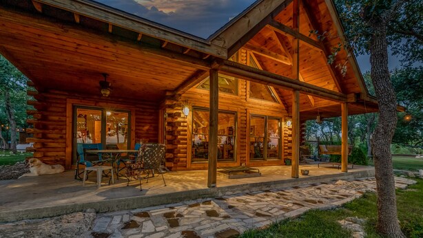 A log cabin with a covered porch, stone pathway, and outdoor seating area. - Hill Country Ranch Retreat, Pool, Views, Sleeps 16+, Weddings & Family Groups (Florence)