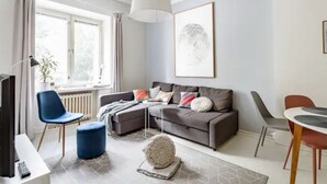 Un saló modern amb un sofà gris, cadires blaves i vermelles, una taula de menjador i una finestra gran amb cortines.