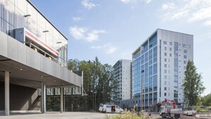 En modern byggnad med ett platt tak och en stor glasfasad, omgiven av träd och andra byggnader.