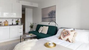 Ett modernt, minimalistiskt vardagsrum med en grön soffa, vita sängkläder och en matplats med vita skåp.