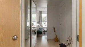En smal hall som leder till ett sovrum med en säng, sängbord och ett fönster.