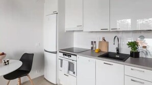 Ett modernt kök med vita skåp, en svart bänkskiva, en diskho och en matplats med en svart stol och ett litet bord.