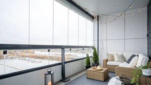Un balcón con vista a un cuerpo de agua, mobiliario de mimbre y luces colgantes.