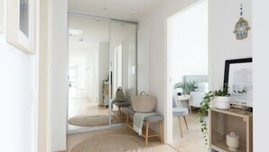 Una habitación moderna y bien iluminada con un vidrio que da a otro espacio, un tapete redondo, una silla con cojín y una estantería con una planta.