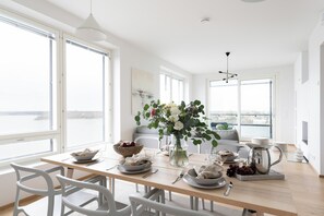 Een moderne eetruimte met een houten tafel gedekt voor twee personen, witte stoelen en uitzicht op de stad door grote ramen.