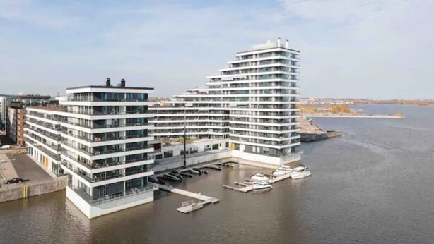 Un hotel moderno de varios pisos con vista al agua, con balcones y un puerto deportivo con barcos.