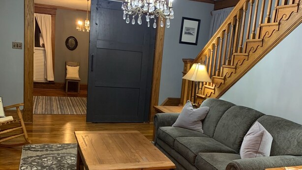 A cozy living room with a wooden coffee table, a grey sofa, and a staircase with wooden railings. - Charming 3-bedroom house in lovely downtown Madison. (Madison)
