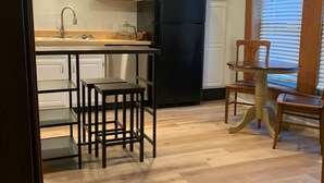 A kitchen with white cabinets, a black refrigerator, a wooden dining table with two chairs, and a window with blinds. - Charming 3-bedroom house in lovely downtown Madison. (Madison)
