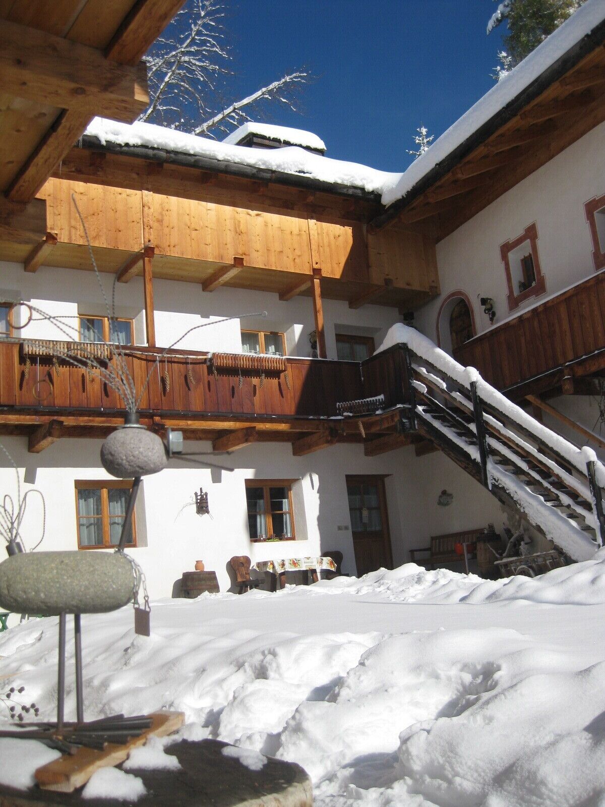 Un chalet en bois doté d’un balcon, d’un escalier et d’un toit recouvert de neige.