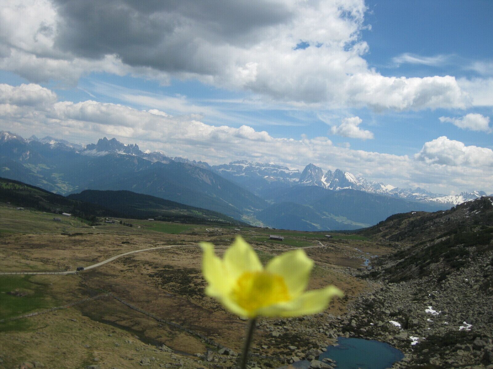 Paesaggio montuoso con cielo sereno, una strada e un piccolo specchio d'acqua.