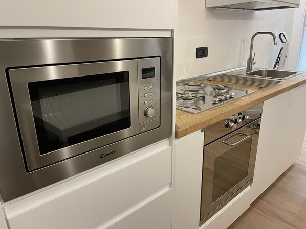 Een compacte keuken met een inbouwmagnetron, een roestvrijstalen fornuis en een houten aanrecht.