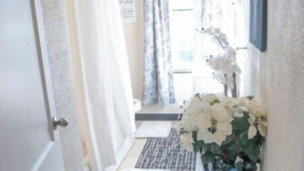 A narrow hallway with a tiled floor, a white door, a small rug, a black trash bin, and a vase with white flowers. - 2BR 1B APT MINS TO DOWNTOWN (Pittsburgh)