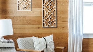 Ein gemütliches Zimmer mit Holzboden, einem gemusterten Teppich, einer Couch, einem Sessel und dekorativen Wandverkleidungen.