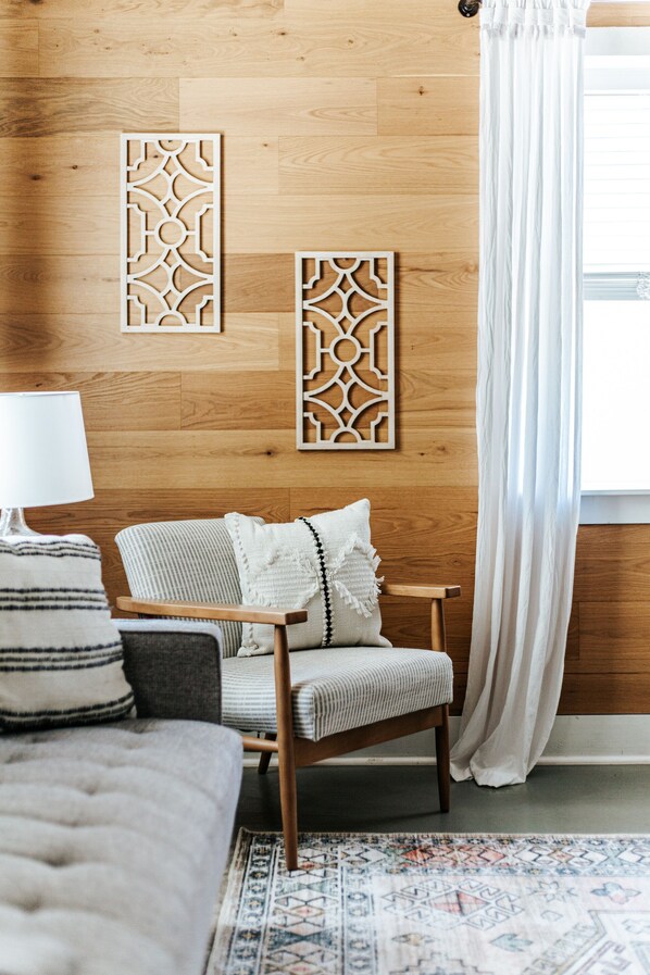 Une pièce chaleureuse avec un plancher en bois, un tapis à motifs, un canapé, un fauteuil et des panneaux décoratifs sur les murs.