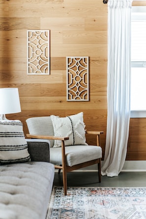 Une pièce chaleureuse avec un plancher en bois, un tapis à motifs, un canapé, un fauteuil et des panneaux décoratifs sur les murs.