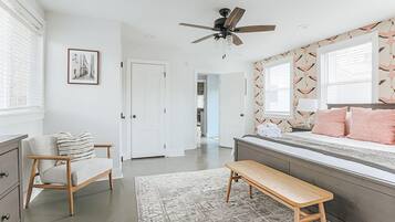 A bedroom with a bed, a bench, a chair, a ceiling fan, and a door.