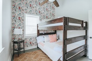 Un lit superposé avec une structure en bois, une table de chevet avec une lampe et un papier peint à motifs floraux.