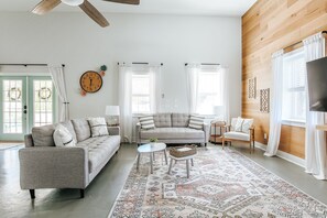 A spacious living room with a grey sofa, a small round table, and a patterned rug.