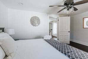A bedroom with a bed, a ceiling fan, a decorative wall piece, and a door leading to another room.