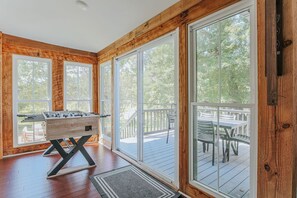 A room with large windows, a wooden deck outside, and a foosball table.