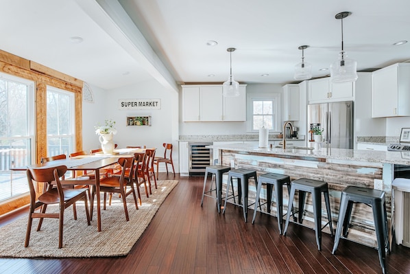 A modern kitchen with white cabinets, a stainless steel refrigerator, and a bar area with stools.