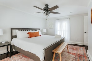 A bedroom with a bed, a wooden bench, a ceiling fan, and a patterned rug.