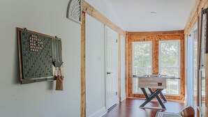 Quarto com piso de madeira, mesa de pebolim e um jogo de tabuleiro fixado na parede.