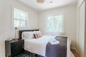 A bedroom with a bed, a bedside table, and two windows.