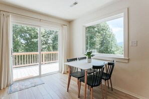 A dining area with a table and chairs, large windows, and a view of trees.
