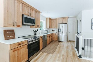 A modern kitchen with wooden cabinets, stainless steel appliances, and a welcome sign.
